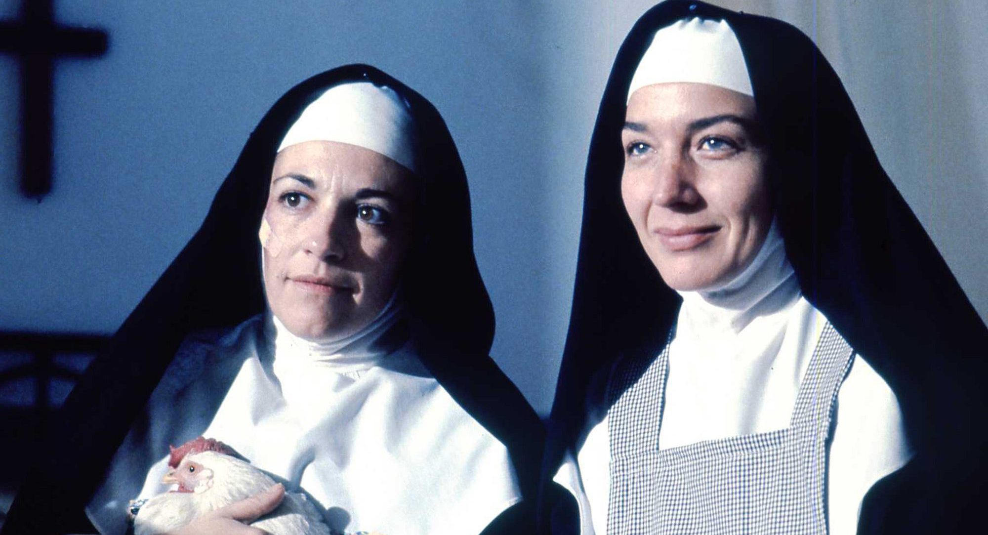 Two smiling nuns stand side by side, one holding a chicken.