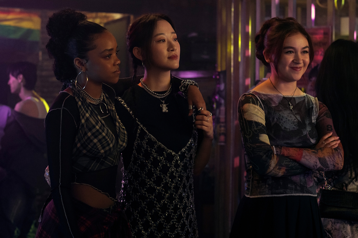 XO, Kitty season two: The roomies share a night out! Juliana drapes her arm around Yuri as Kitty stands nearby, looking at something off-screen,