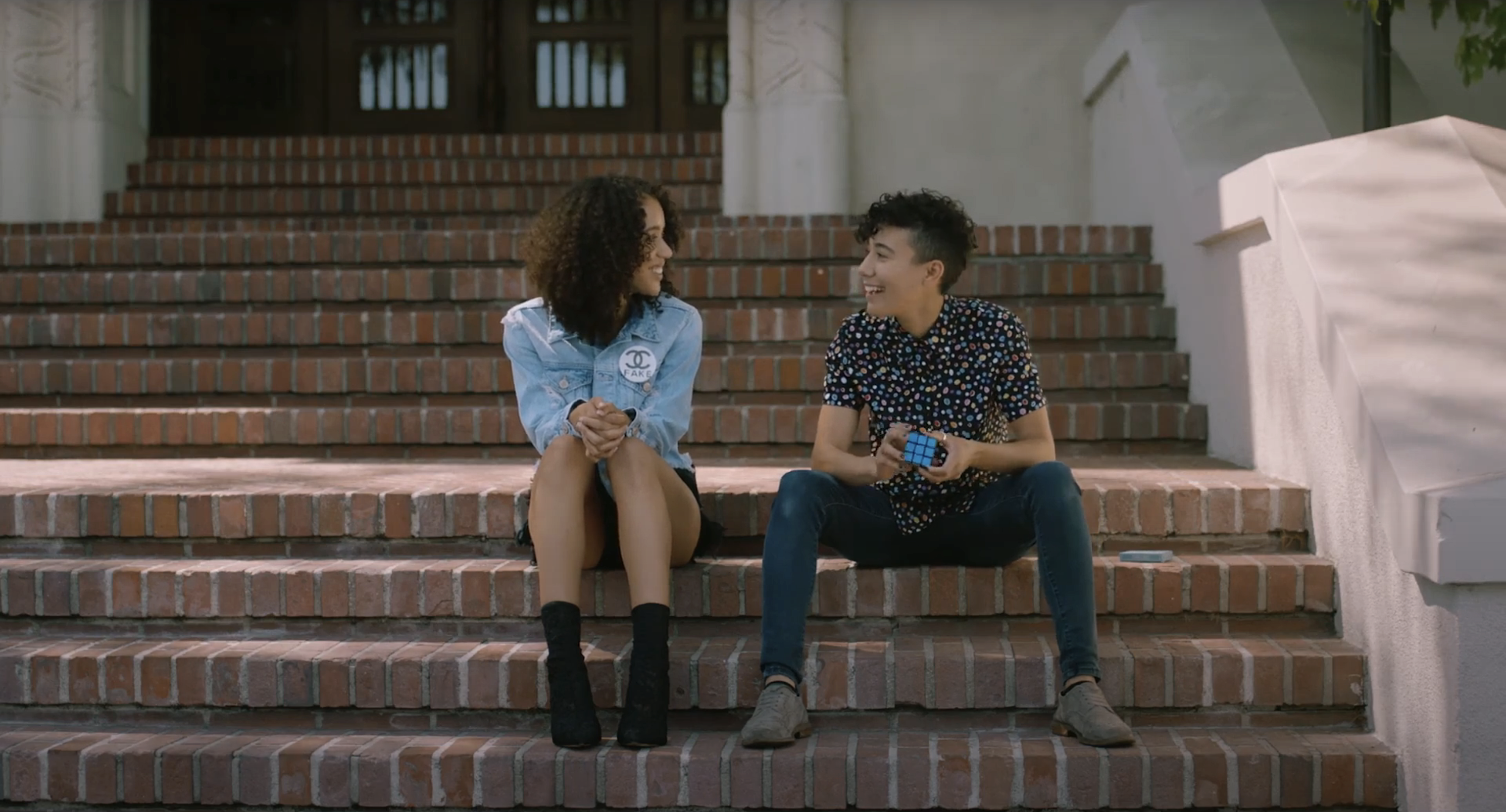 Jasmin Savoy Brown and Vico Ortiz talk while sitting on some stairs.
