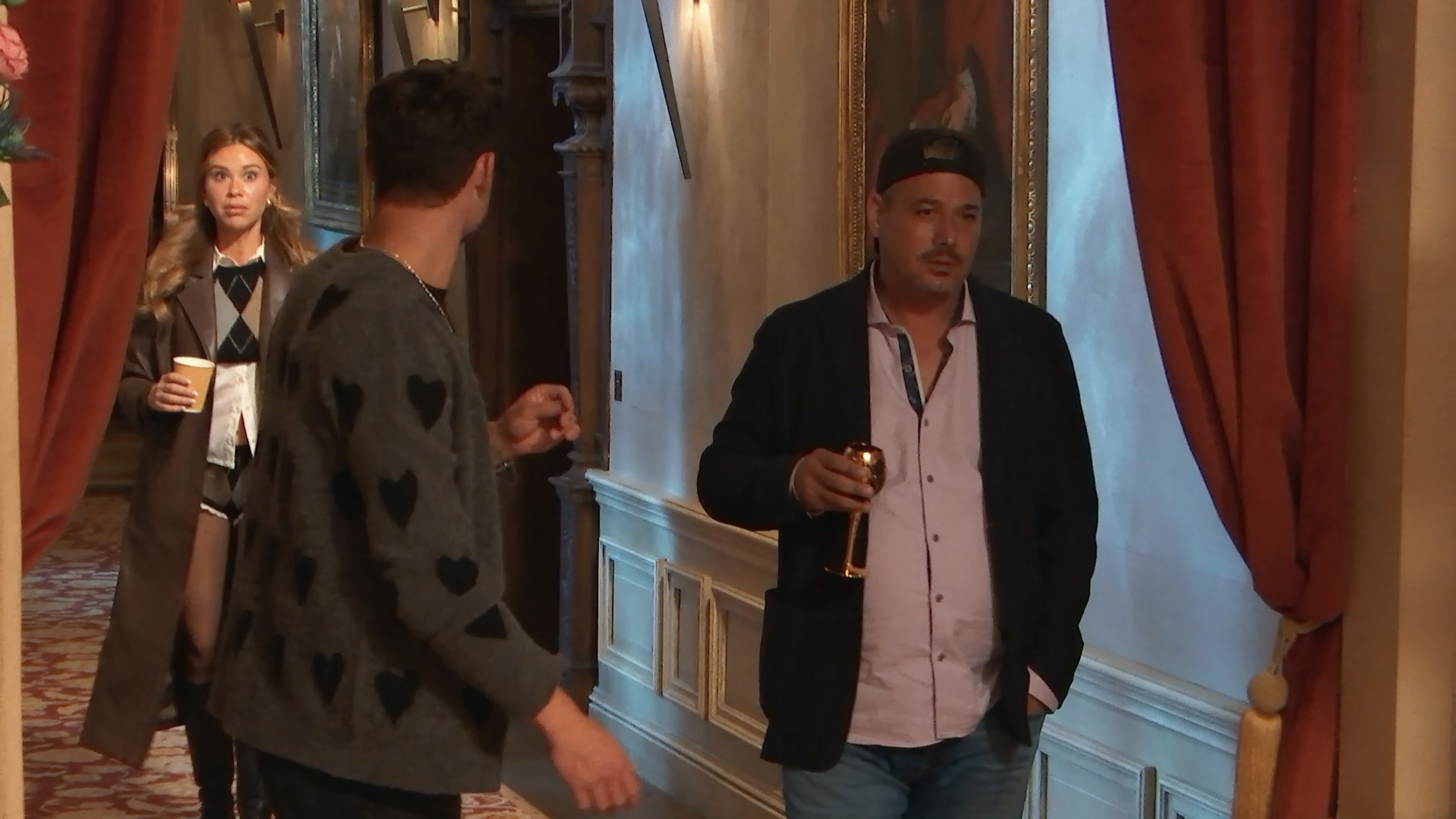 Gabby in a tiny argyle sweater/short set and a long brown coat looks surprised seeing Dylan and Rob