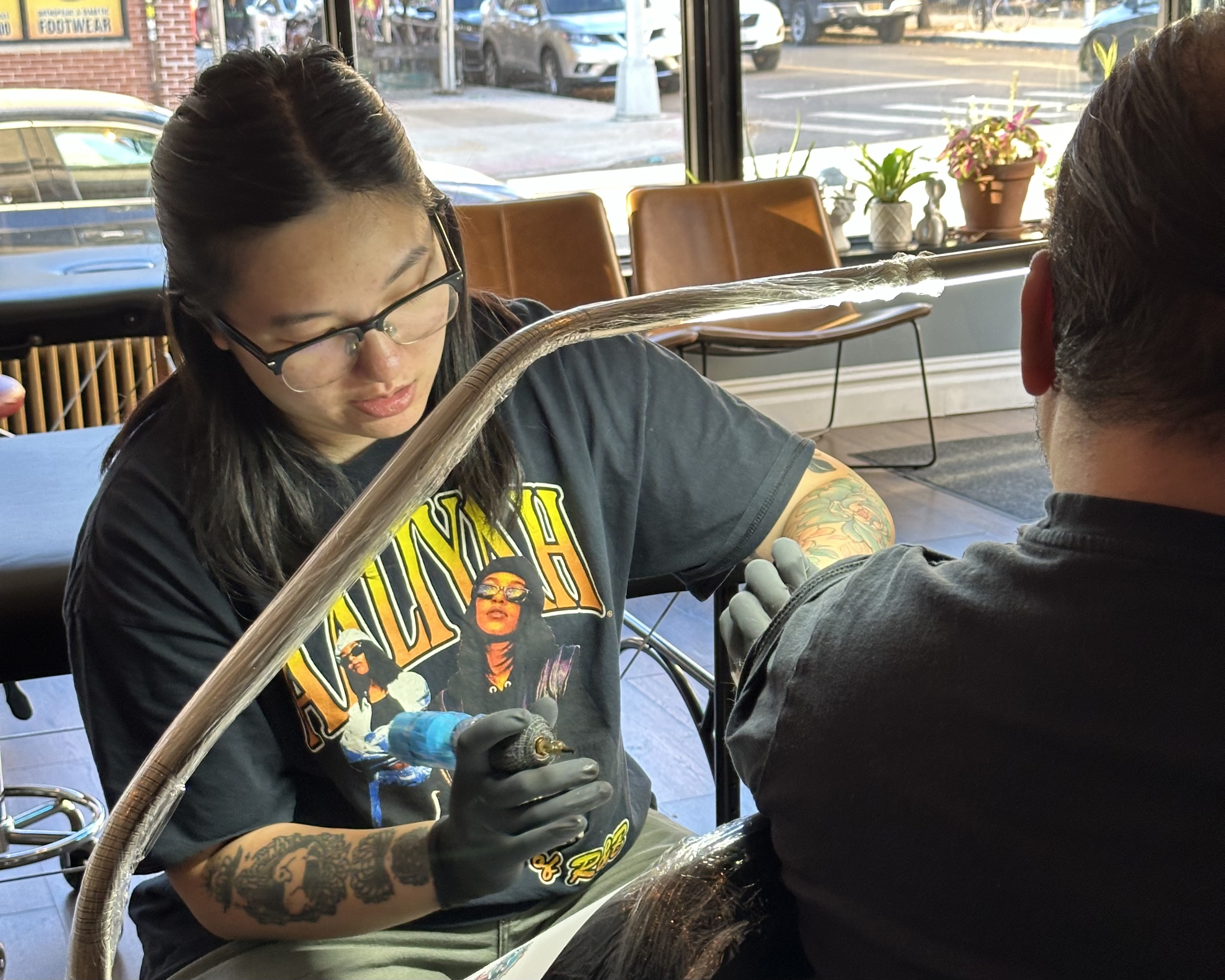 Tiffany Lai works on a tattoo while wearing an Aaliyah shirt