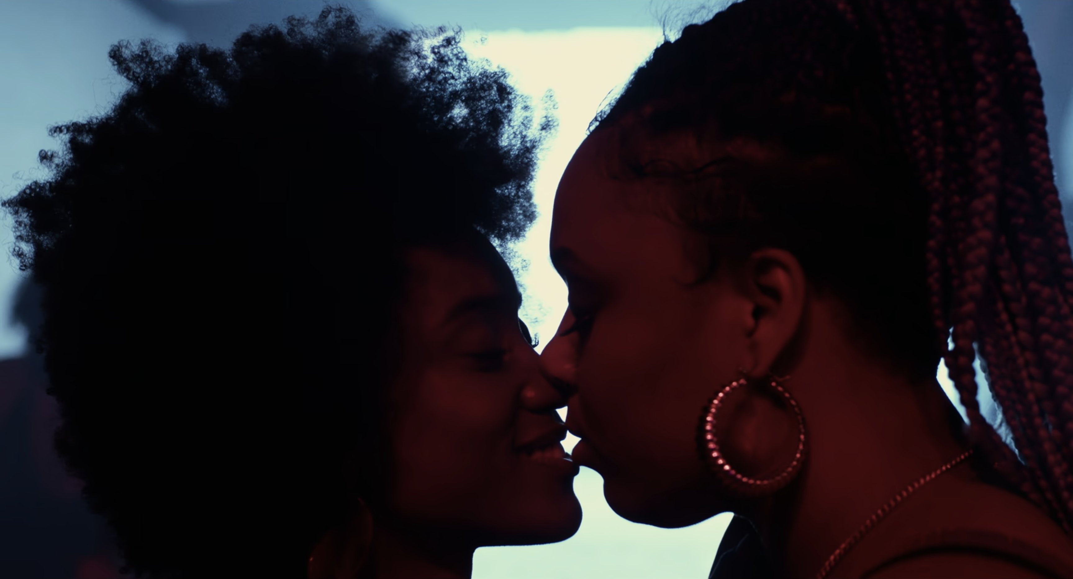 The best lesbian club scenes: Two women kiss in a club with a glowing blue light behind them
