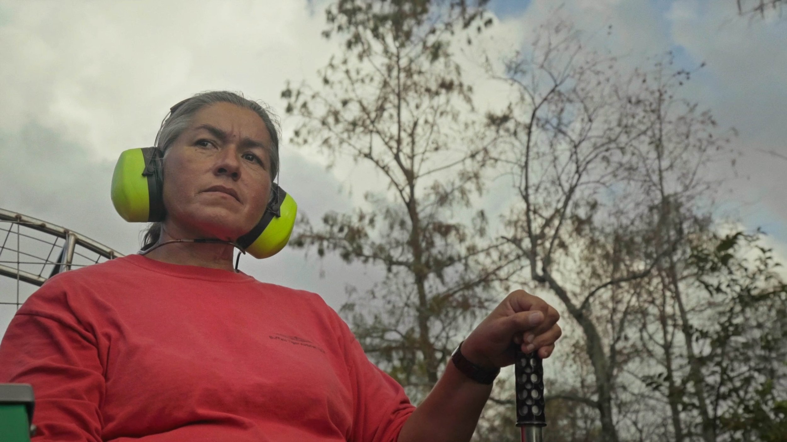 Betty Osceola in an orange shirt and ear covers in River of Grass