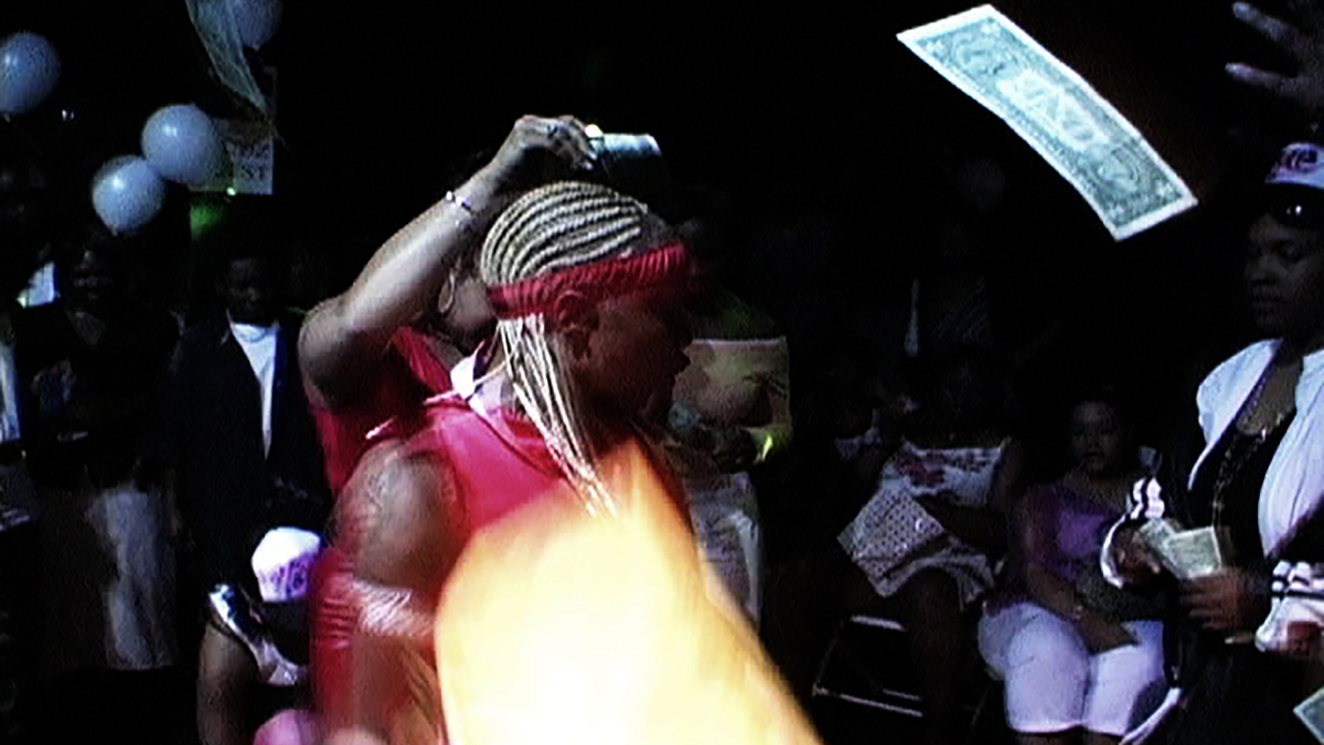 A still from Shakedown of a stud dancing with a dollar bill in the air