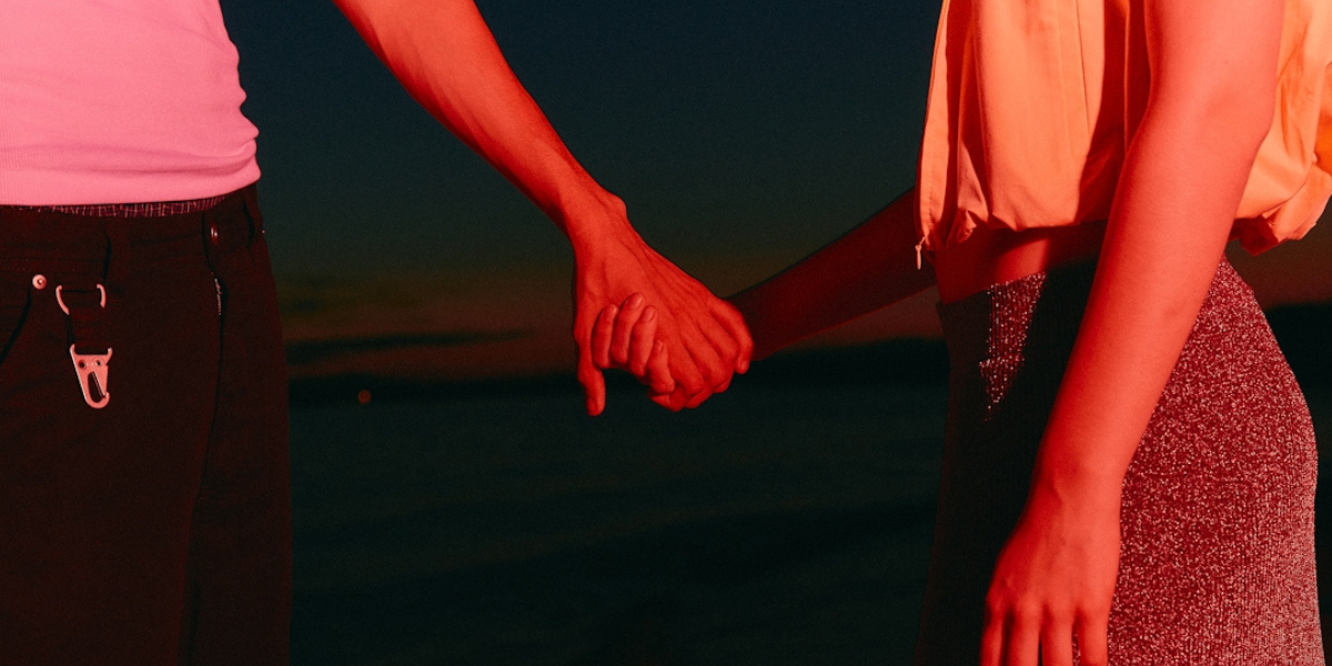 a masc person and a femme person holding hands