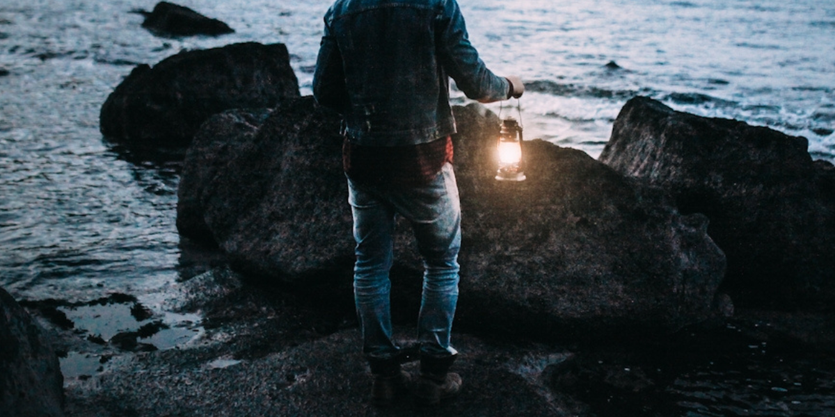 a person with a lantern looking out to sea