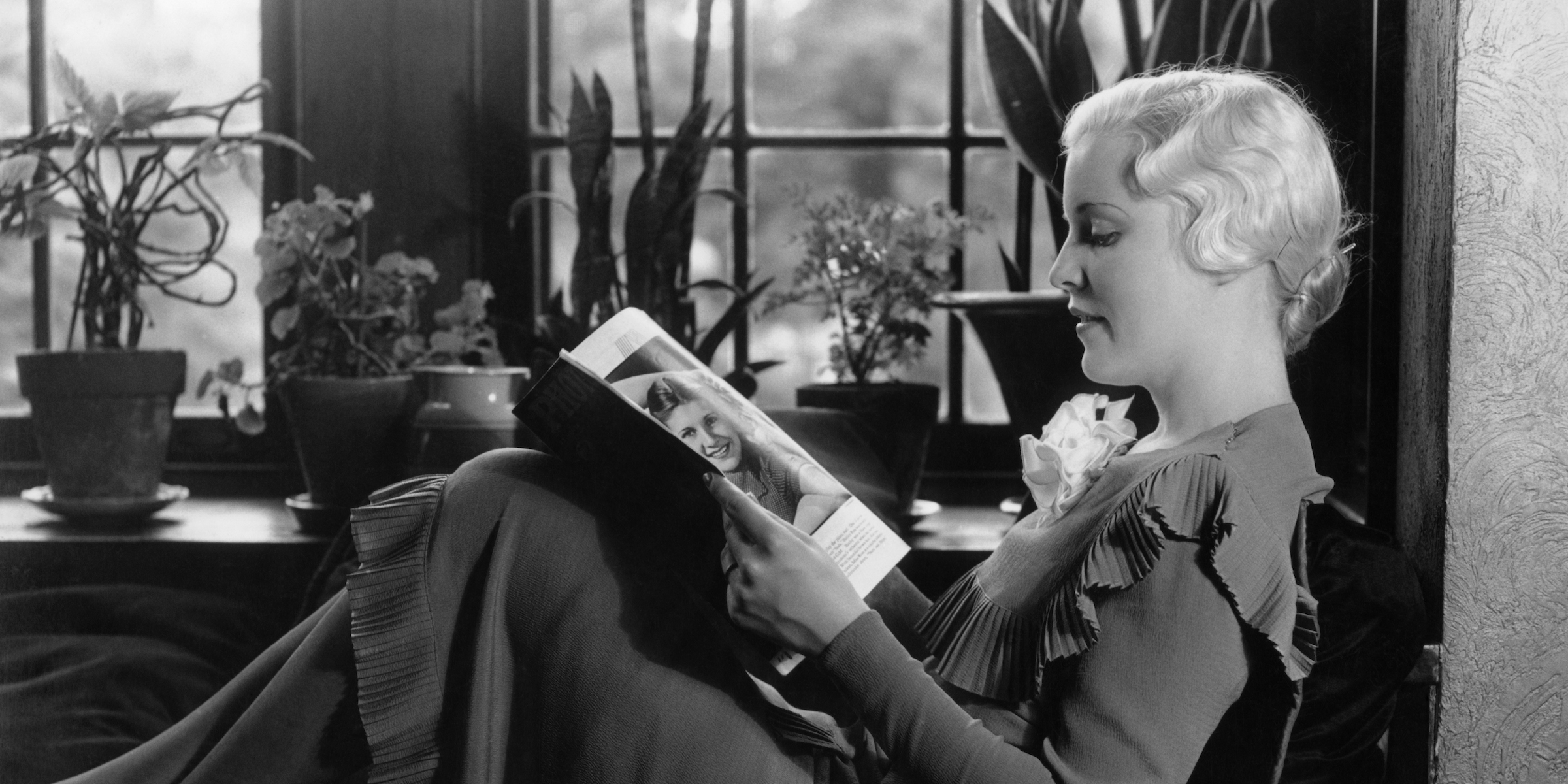 1930s BLOND WOMAN SITTING BY WINDOW READING MAGAZINE PROFILE VIEW PLANTS IN BACKGROUND WINDOW SEAT (Photo by H. Armstrong Roberts/ClassicStock/Getty Images)