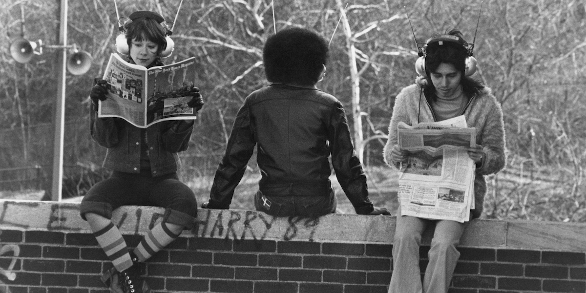 Three girls, each wearing headphones as they sit on a wall, with one reading from a magazine while the other reads from a newspaper in Central Park, in the Manhattan borough of New York City, New York, 7th April 1972. (Photo by Daily Express/Archive Photos/Getty Images)