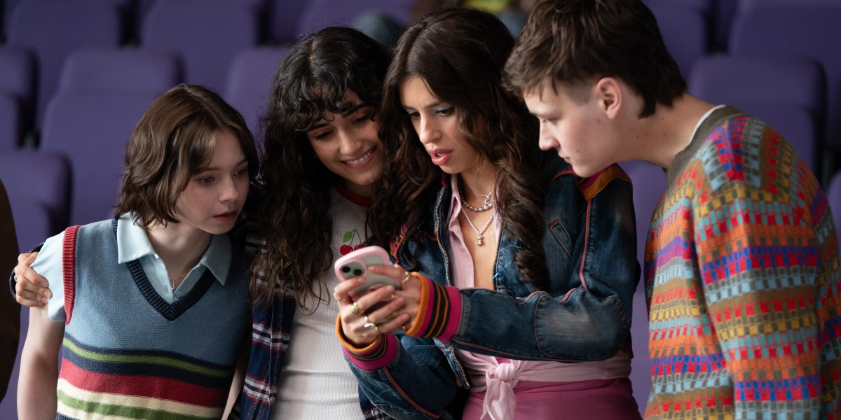 Press still of A Good Girl's Guide to Murder featuring Pip, Cara, Lauren, and Connor all looking at a cell phone together. Photo courtesy of Netflix.