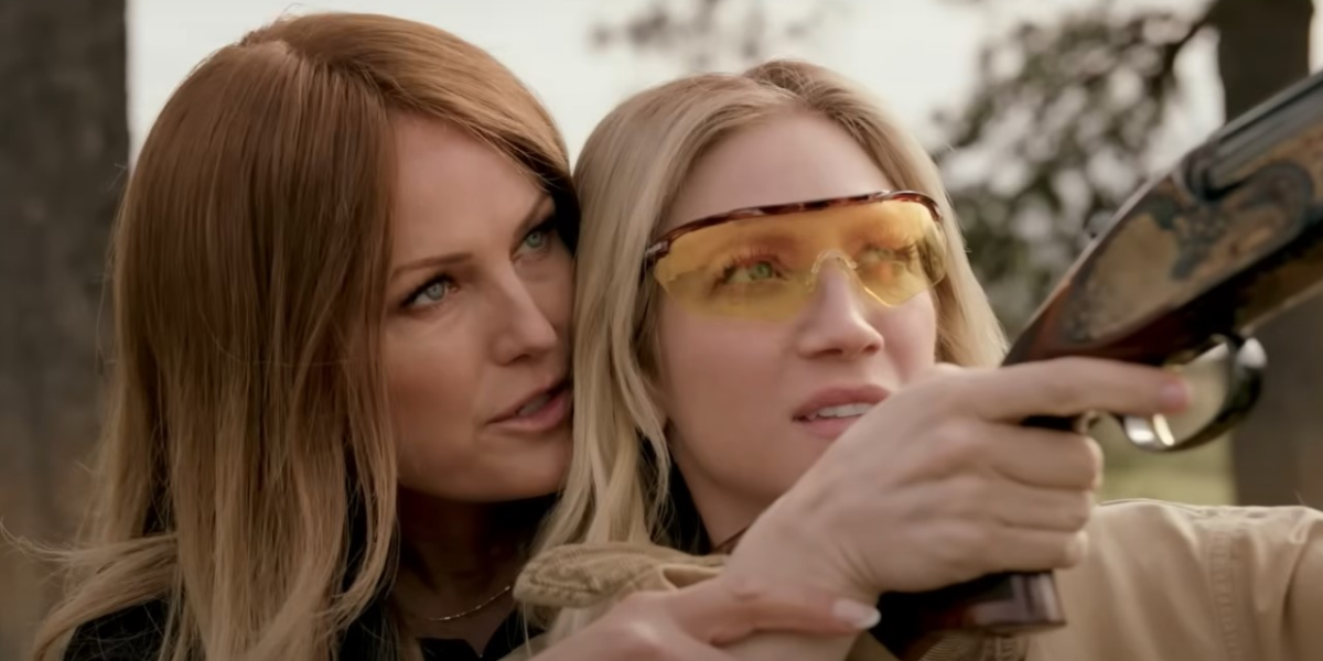 Still from Hunting Wives: Margo standing behind Sophie sensually teaching her how to shoot a gun